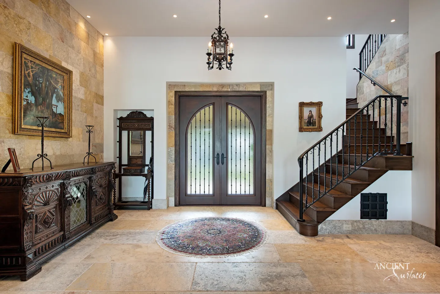 Entrance hall with large pale limestone floor slabs, a feature wall clad in gold and grey limestone blocks, a limestone surround around arched double doors and a timber staircase