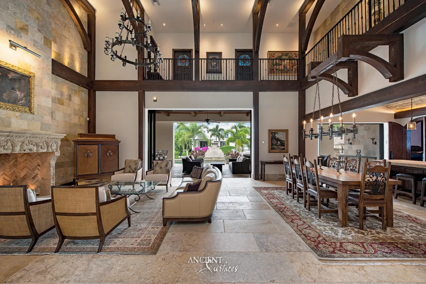 Double height great room with large pale limestone floor slabs running from a carved stone fireplace and limestone clad wall to the dining table