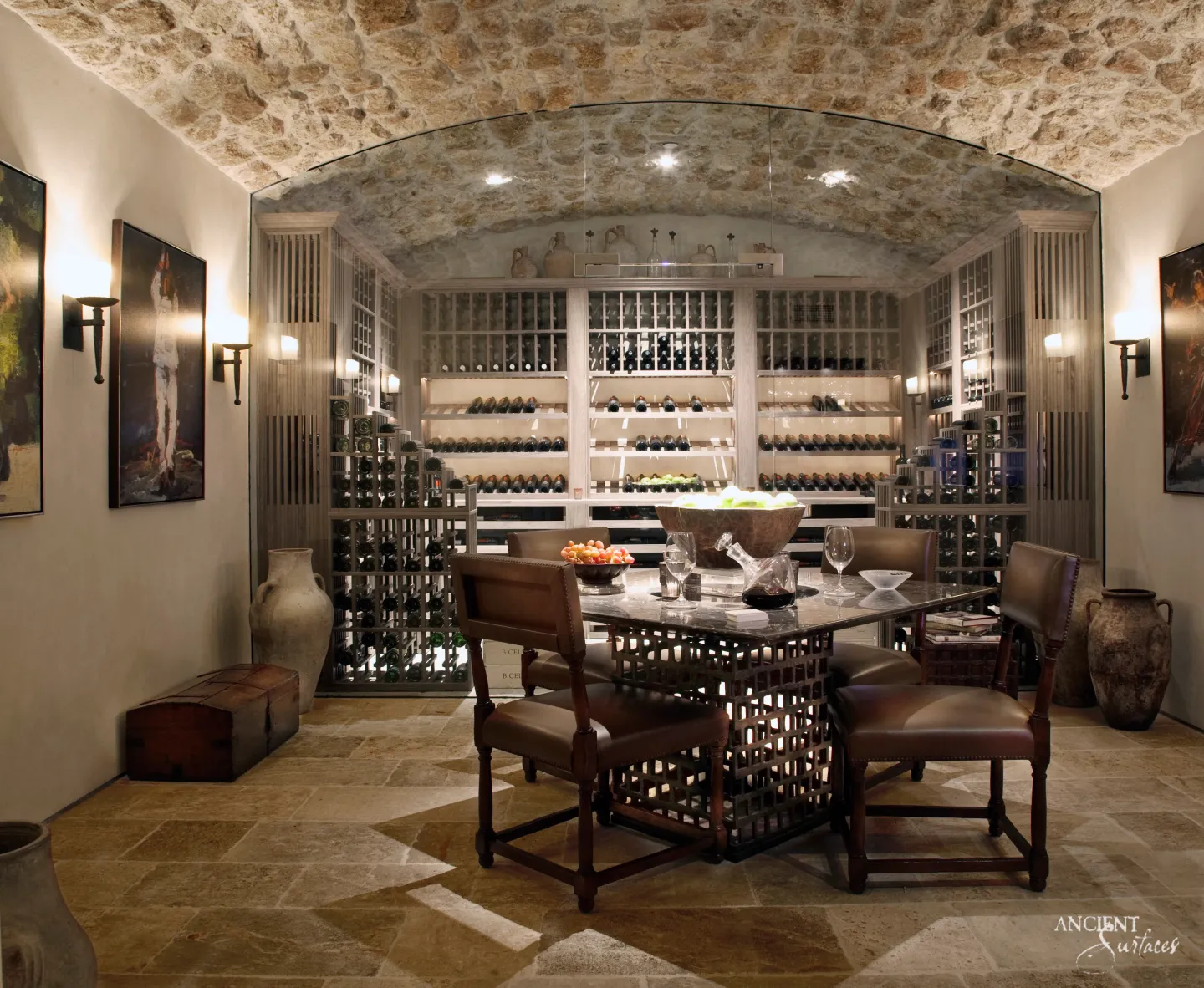 Wine cellar and tasting room with large worn limestone floor slabs, a rough stone barrel vault, a glass wall before the wine racks and a table with leather chairs