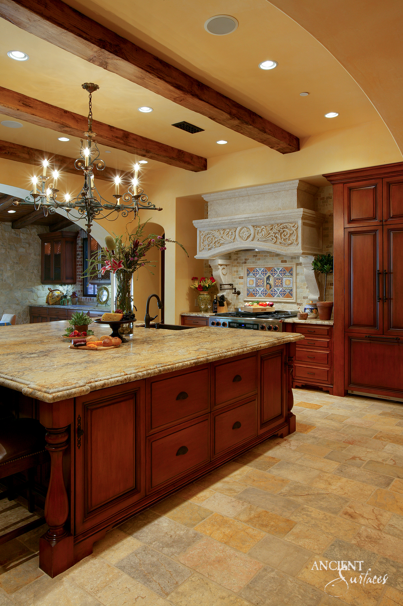 Kitchen with a carved limestone range hood featuring a scrolling acanthus frieze on scrolled corbels, above a tumbled limestone floor in honey and grey