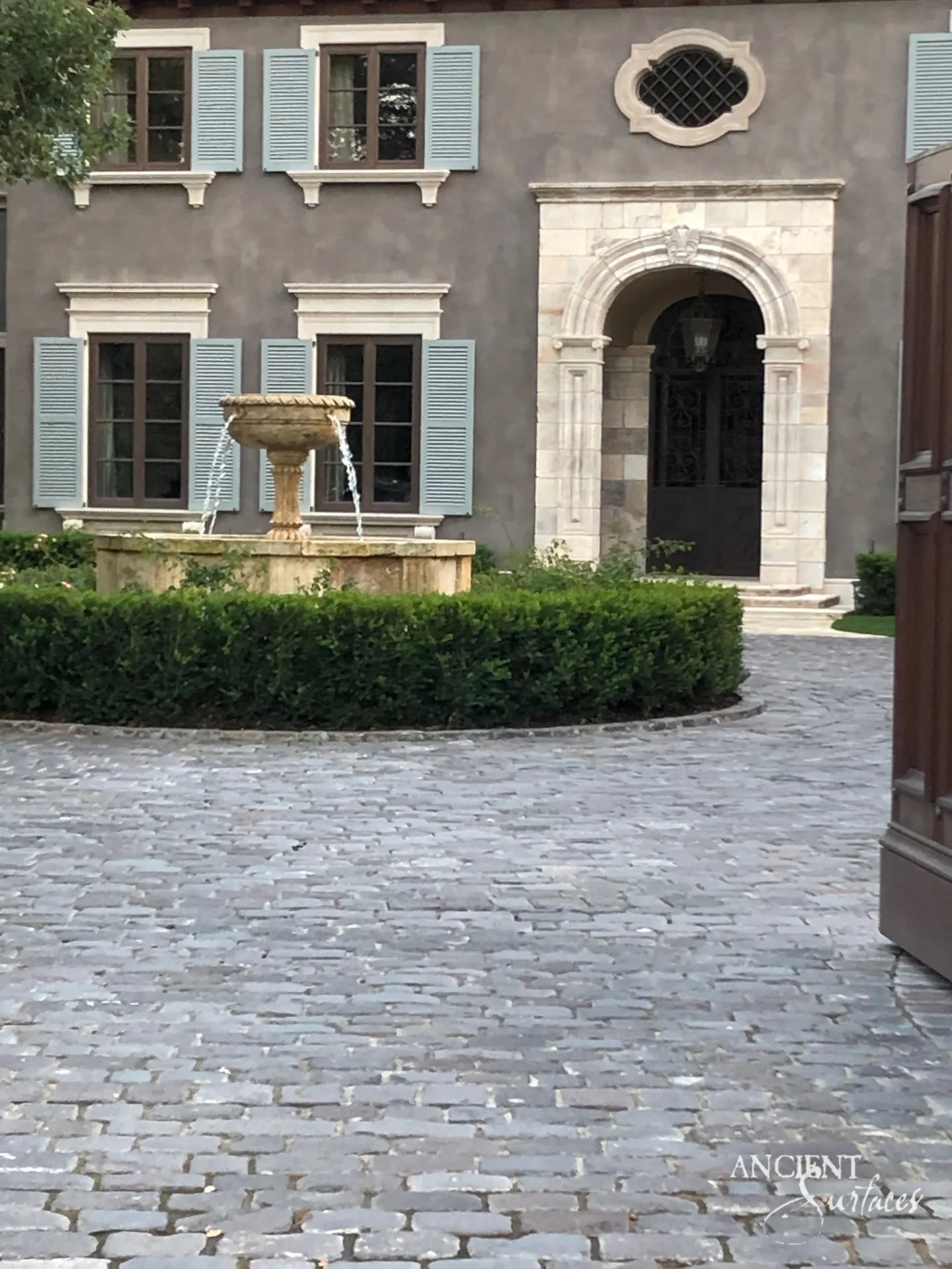 Rendered villa facade with a carved limestone arched entrance, shell keystone and panelled pilasters within cream and rose ashlar, limestone window surrounds with corbelled sills and a cobbled forecourt