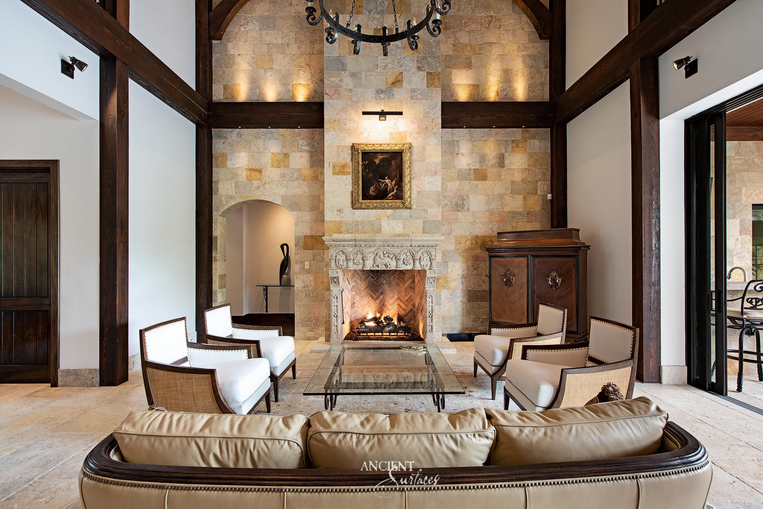Carved stone fireplace with an arcaded figurative frieze set into a full height chimney wall clad in cream, honey and rose limestone blocks, with uplights along a timber ledge