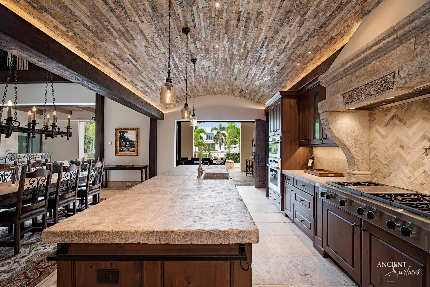 Kitchen with a barrel vaulted ceiling lined in narrow limestone strips, a thick rough edged limestone island top, a carved limestone range hood and a herringbone stone backsplash