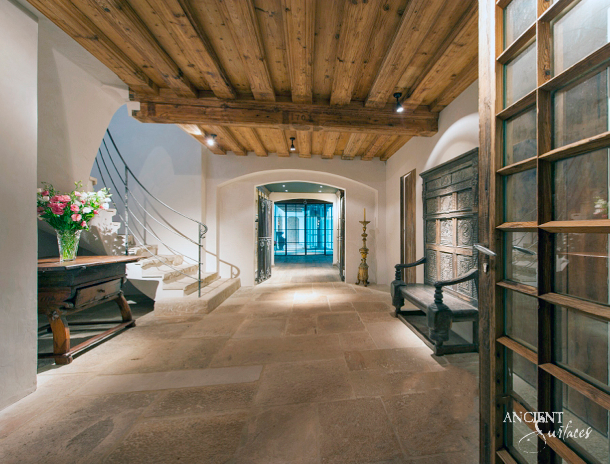 Lower level hall paved in large worn limestone slabs of sand, ochre and grey, with a curved stair of thick stone treads, whitewashed arches and a timber ceiling leading to a glazed room