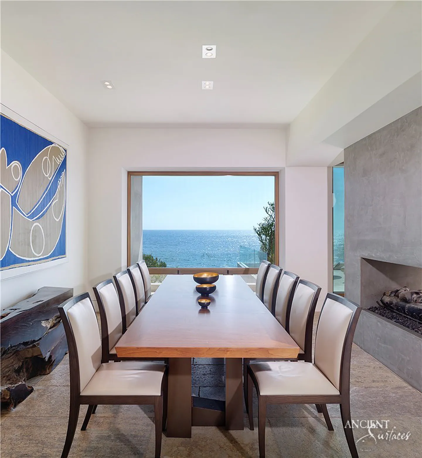 Contemporary dining room on a textured limestone plank floor in grey and sand, facing a picture window onto the ocean